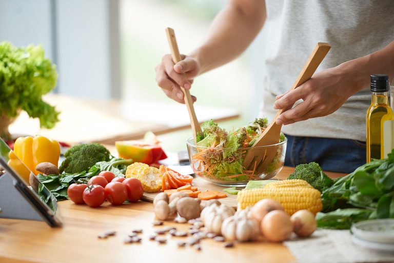 Một người đang trộn salad với nhiều nguyên liệu tốt cho sức khỏe được đặt trên bàn